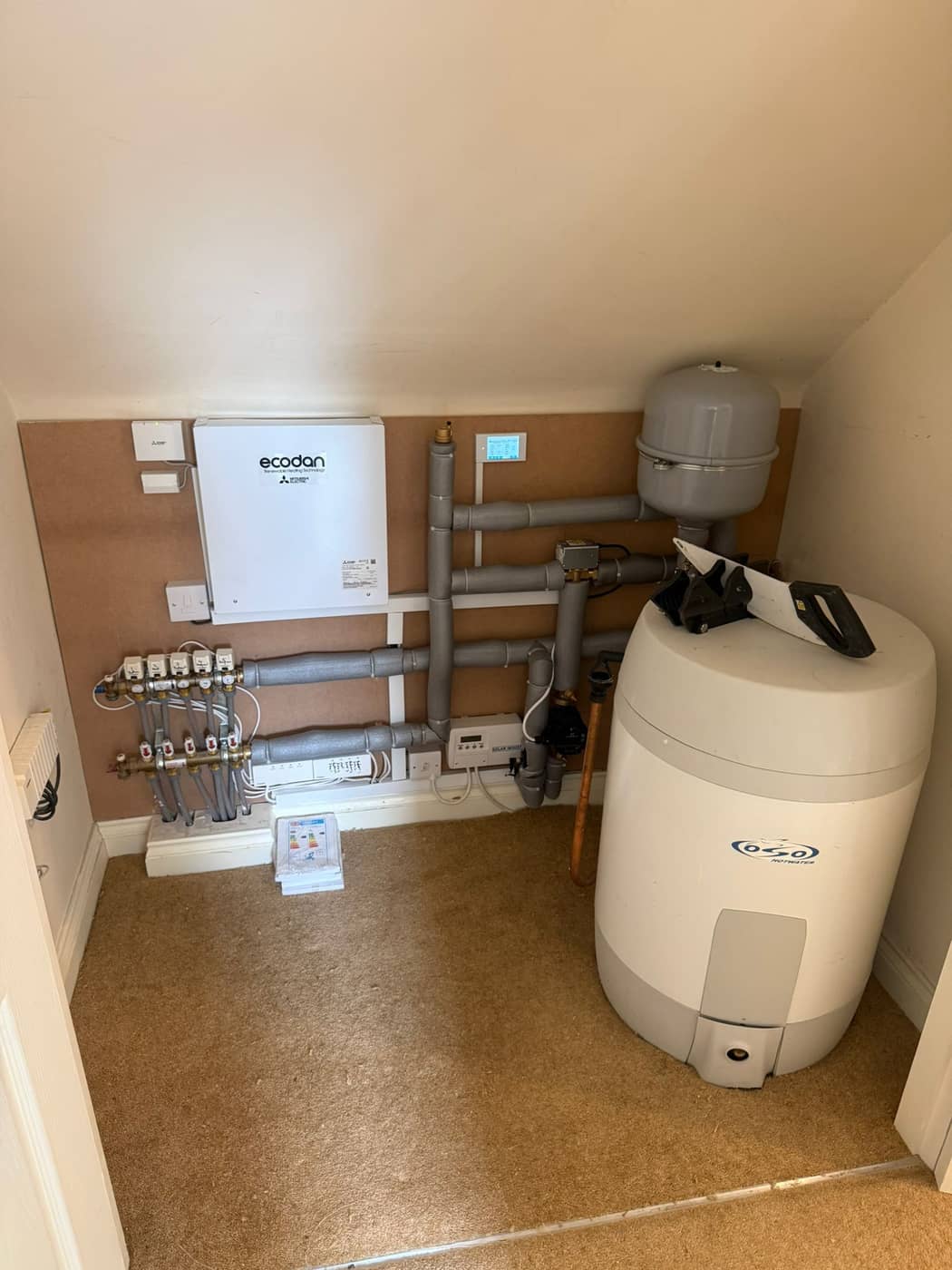 A cupboard fitted with a hot water cylinder, underfloor heating manifold and heat pump controller