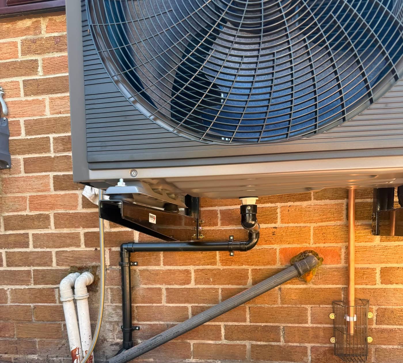 Close-up of a heat pump fan grille and the insulated pipework running along the wall below it