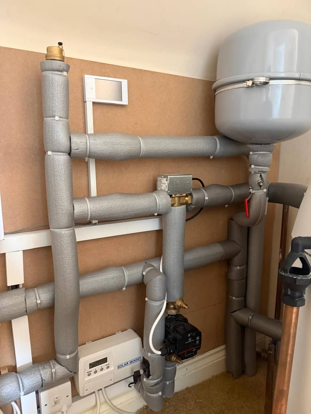 Insulated pipework and a pump neatly fixed to a boarded wall