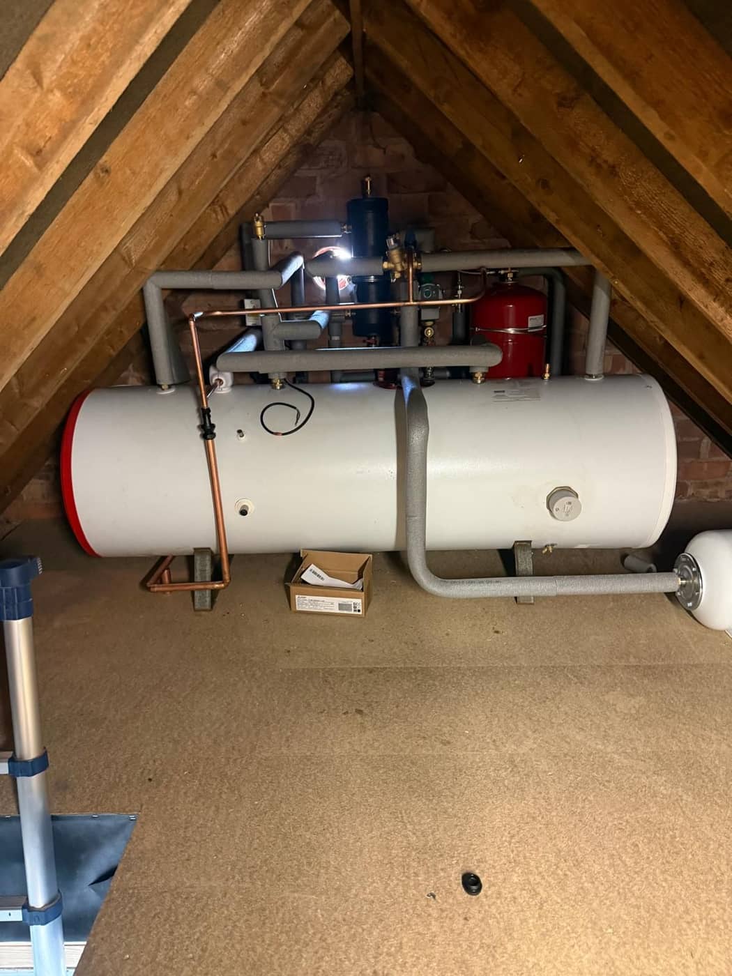 A long horizontal hot water cylinder installed in a boarded loft