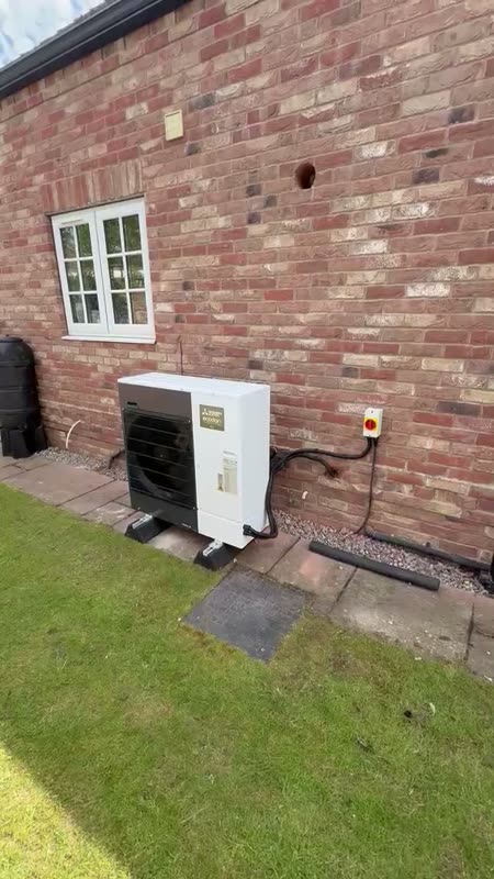 A white Mitsubishi Ecodan heat pump against a brick wall on a sunny day