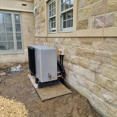 Air conditioning unit beside a stone wall, on a gravelled area.