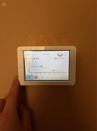 A hand holding a digital thermostat displaying a temperature graph.