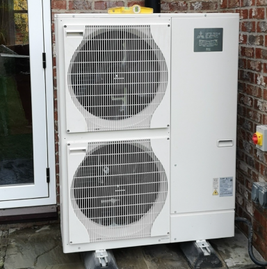 Two stacked air conditioning units outside a brick wall near a glass door.