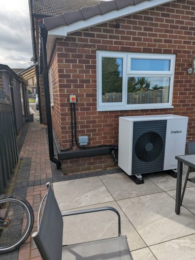 Air source heat pump installed beside a brick wall and patio area.