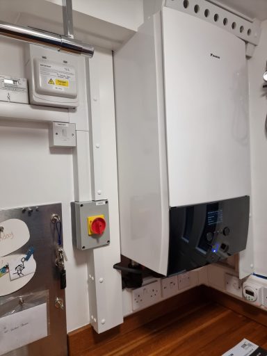 White boiler mounted on a wall, with visible pipes and electrical connections.