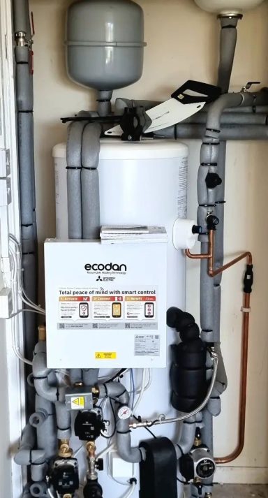 A compact boiler with various pipes and controls mounted on a wall.